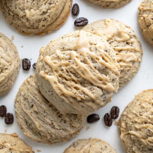 Coffee Sugar Cookies on a Piece of White Parchment Paper Spread out, some Stacked, with Glaze and some Coffee Beans.