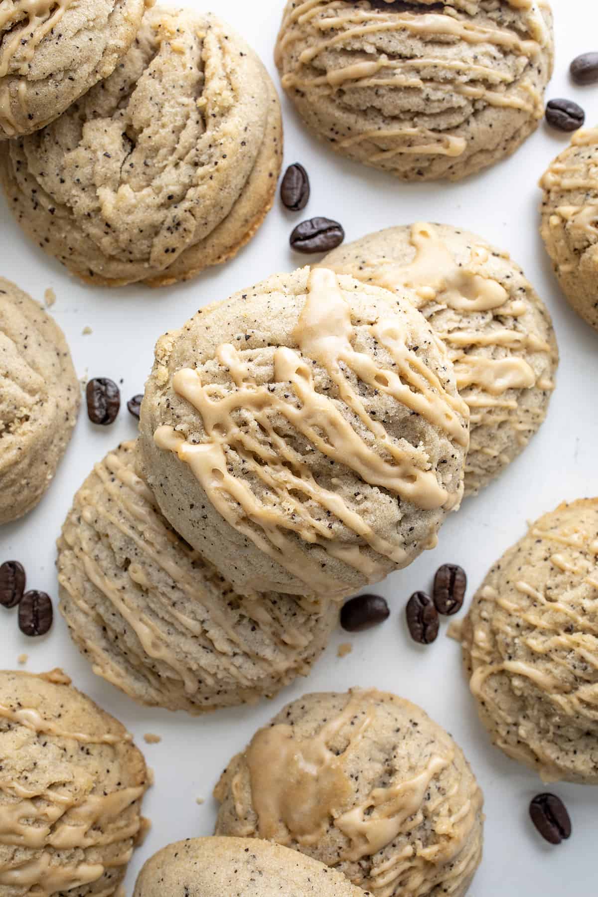 Coffee Sugar Cookies on a Piece of White Parchment Paper Spread out, some Stacked, with Glaze and some Coffee Beans.