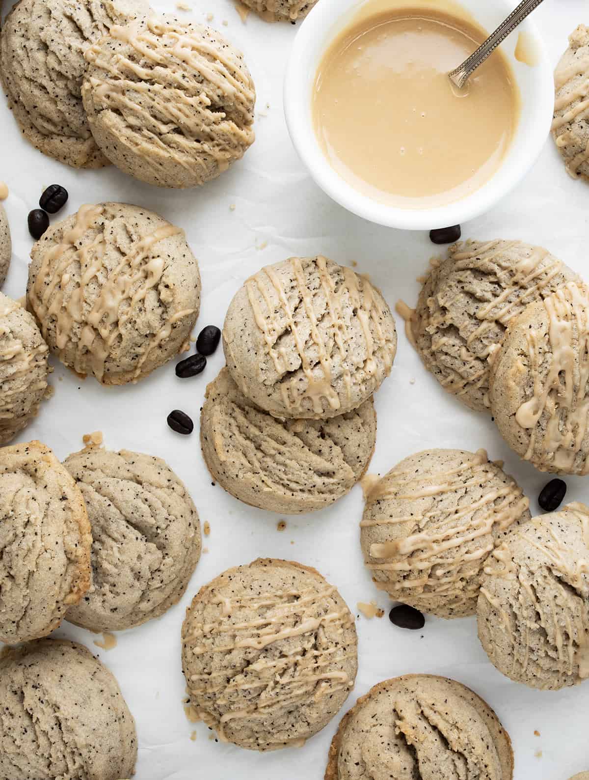 Coffee Sugar Cookies on a Piece of White Parchment Paper Spread out, some Stacked, with Glaze and some Coffee Beans.