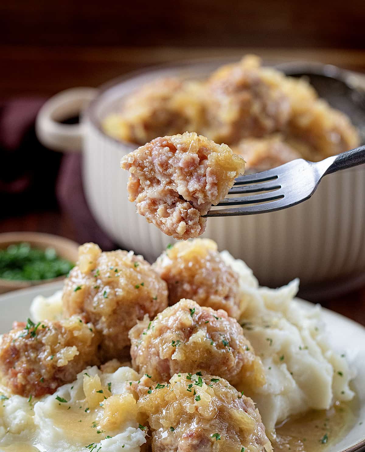 Fork with a Ham Ball on it with a Bite Removed Being Held Over a Plate of Ham Balls on Mashed Potatoes.