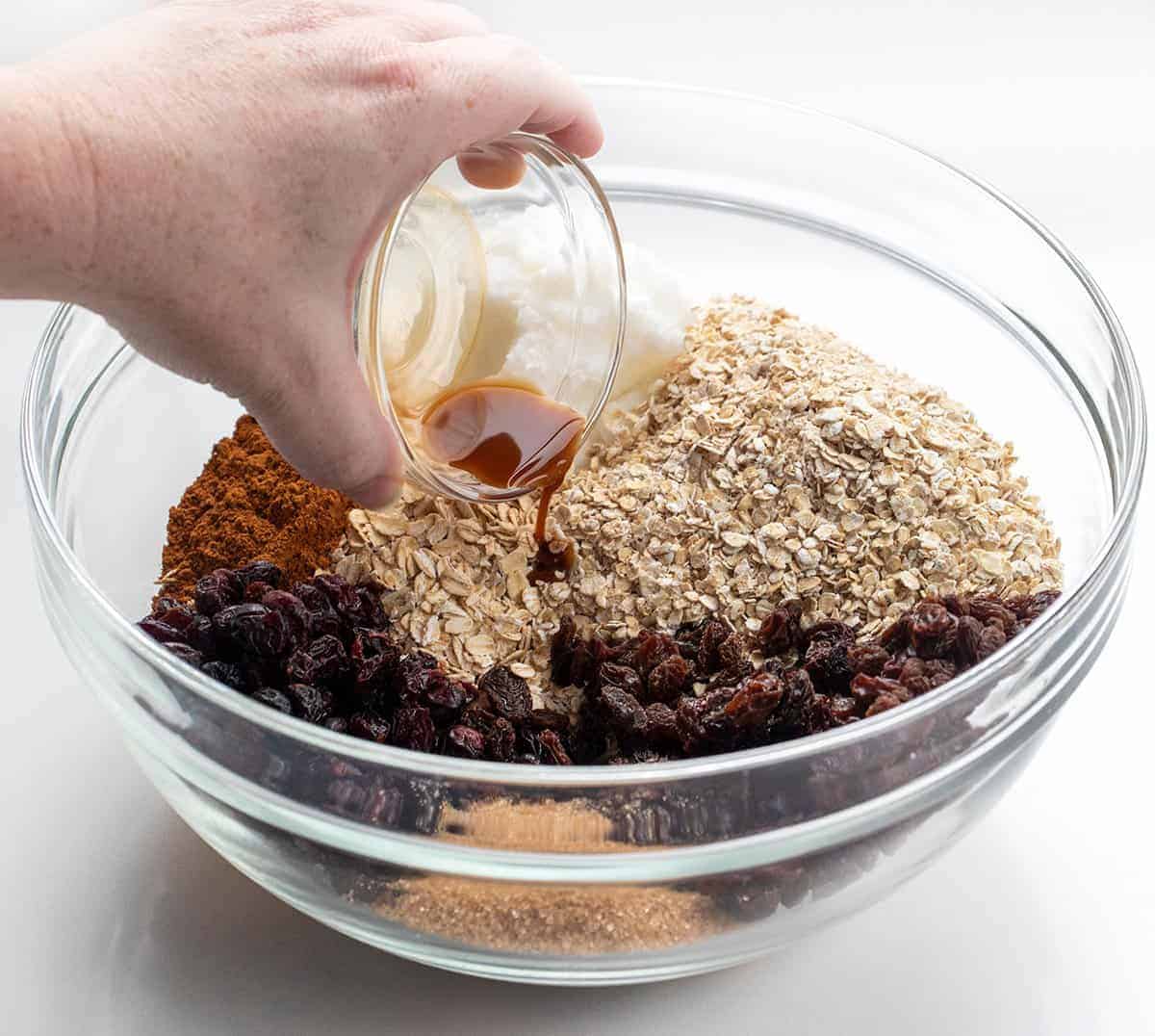 Hand Pouring Vanilla into Raw Ingredients for Homemade Granola