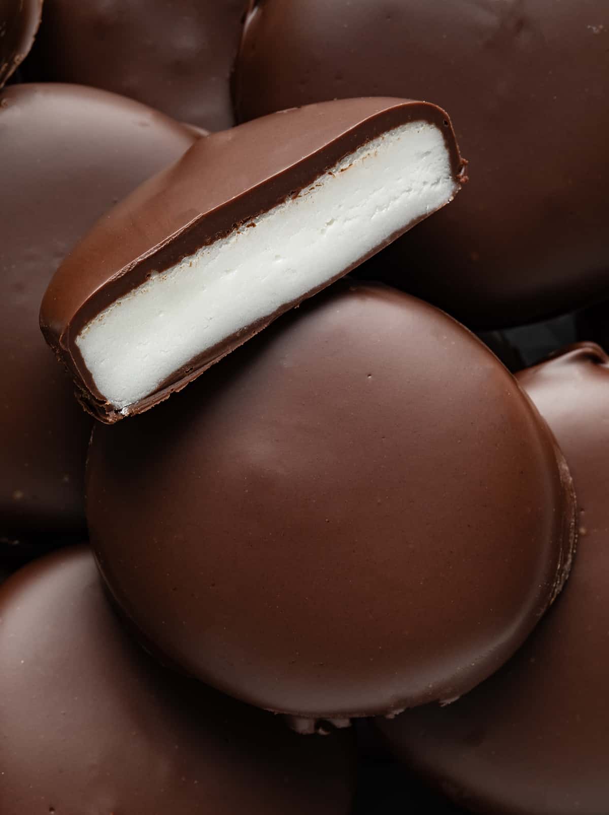 Stack of Homemade Peppermint Patties with top patty halved showing inside.