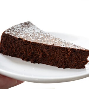 Hand Holding a White Plate with Flourless Chocolate Cake on It.