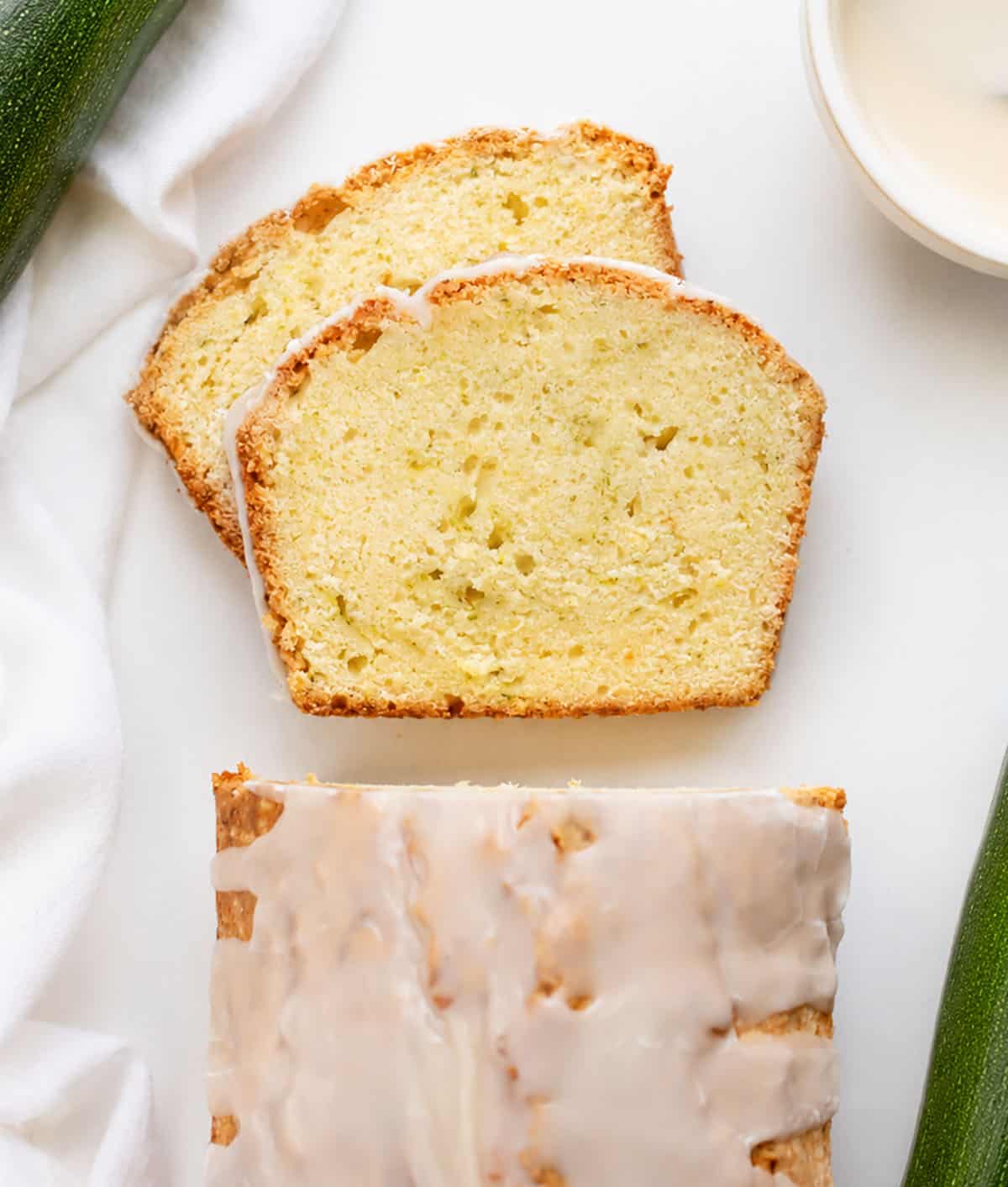Zucchini Pound Cake with slices laying flat on a white table with zucchini.