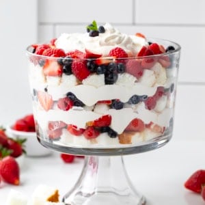 Very Berry Trifle dish on a white counter with fresh fruit like strawberries and blueberries around the base.