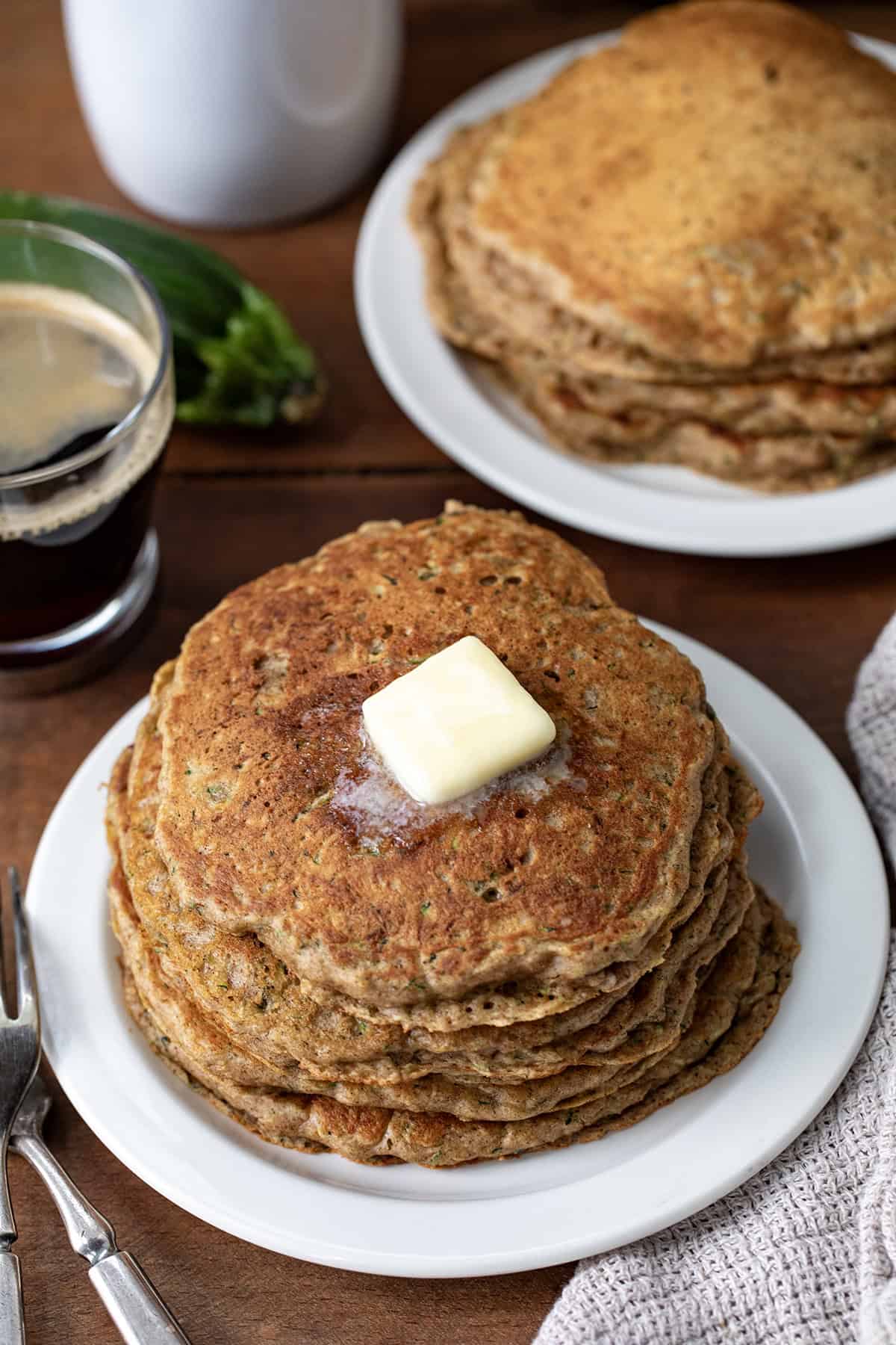 Stacks of Zucchini Pancakes on white plates on a wooden table.