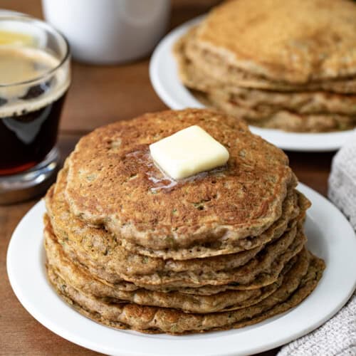 Stacks of Zucchini Pancakes on white plates on a wooden table.