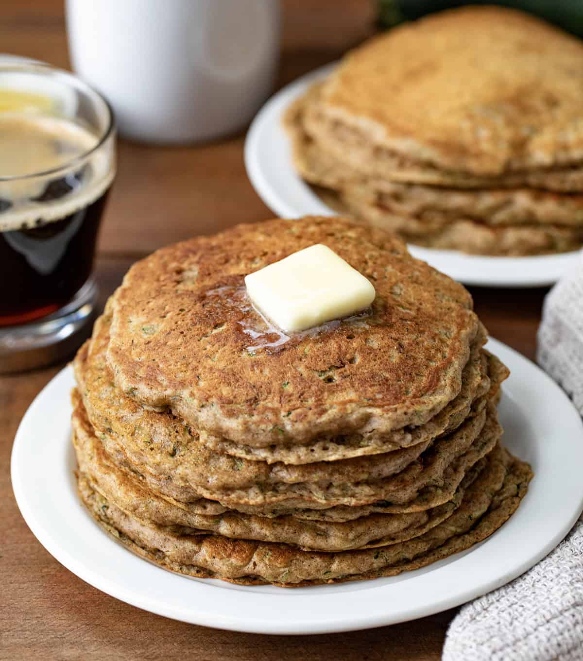 Stacks of Zucchini Pancakes on white plates on a wooden table.