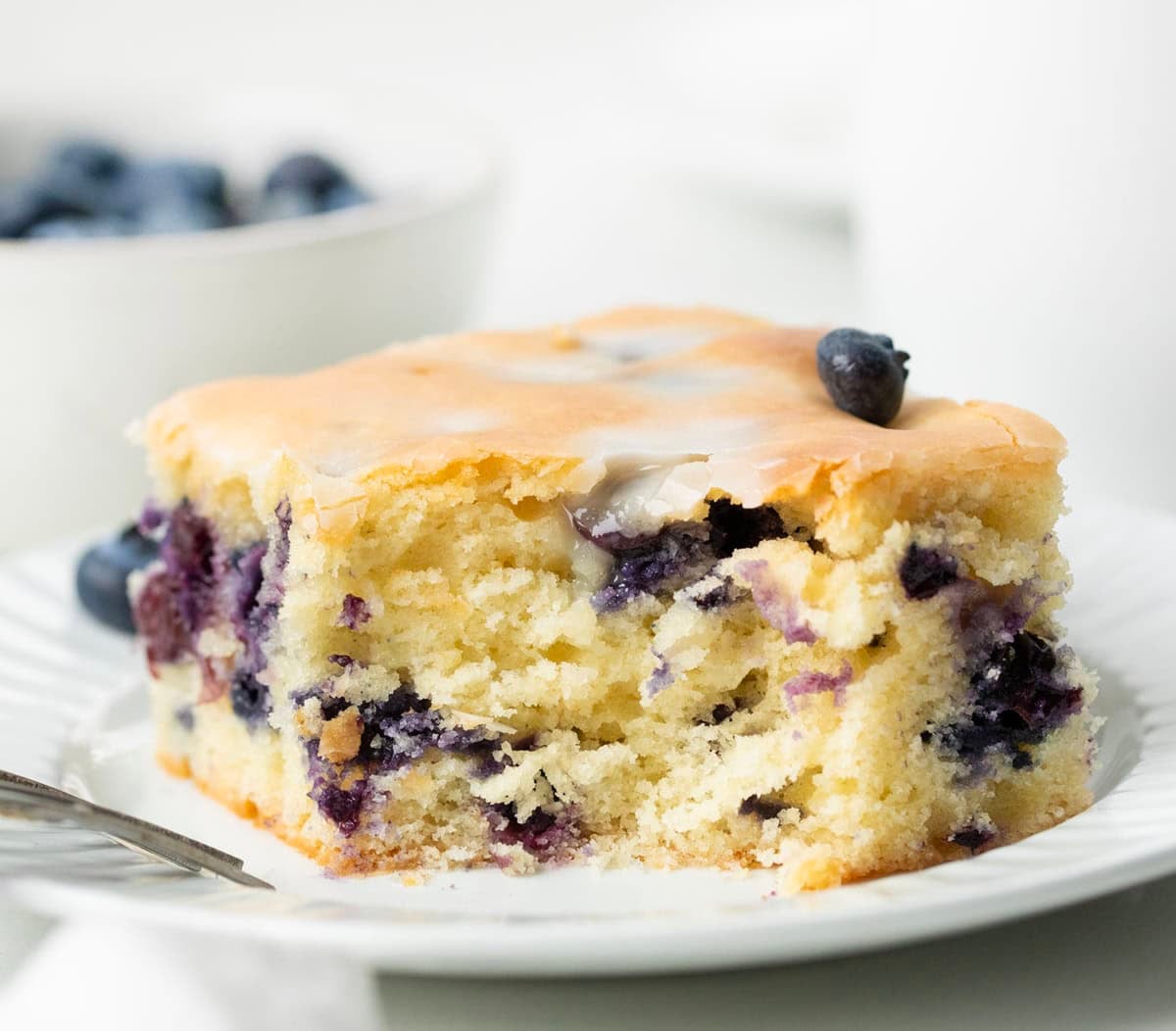 This Blueberry Breakfast Cake is tender, moist, and bursting with sweet, juicy blueberries in every bite! Piece of Blueberry Breakfast Cake with a bite removed showing tender crumb and blueberries inside.