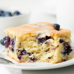 Piece of Blueberry Breakfast Cake with a bite removed showing tender crumb and blueberries inside.