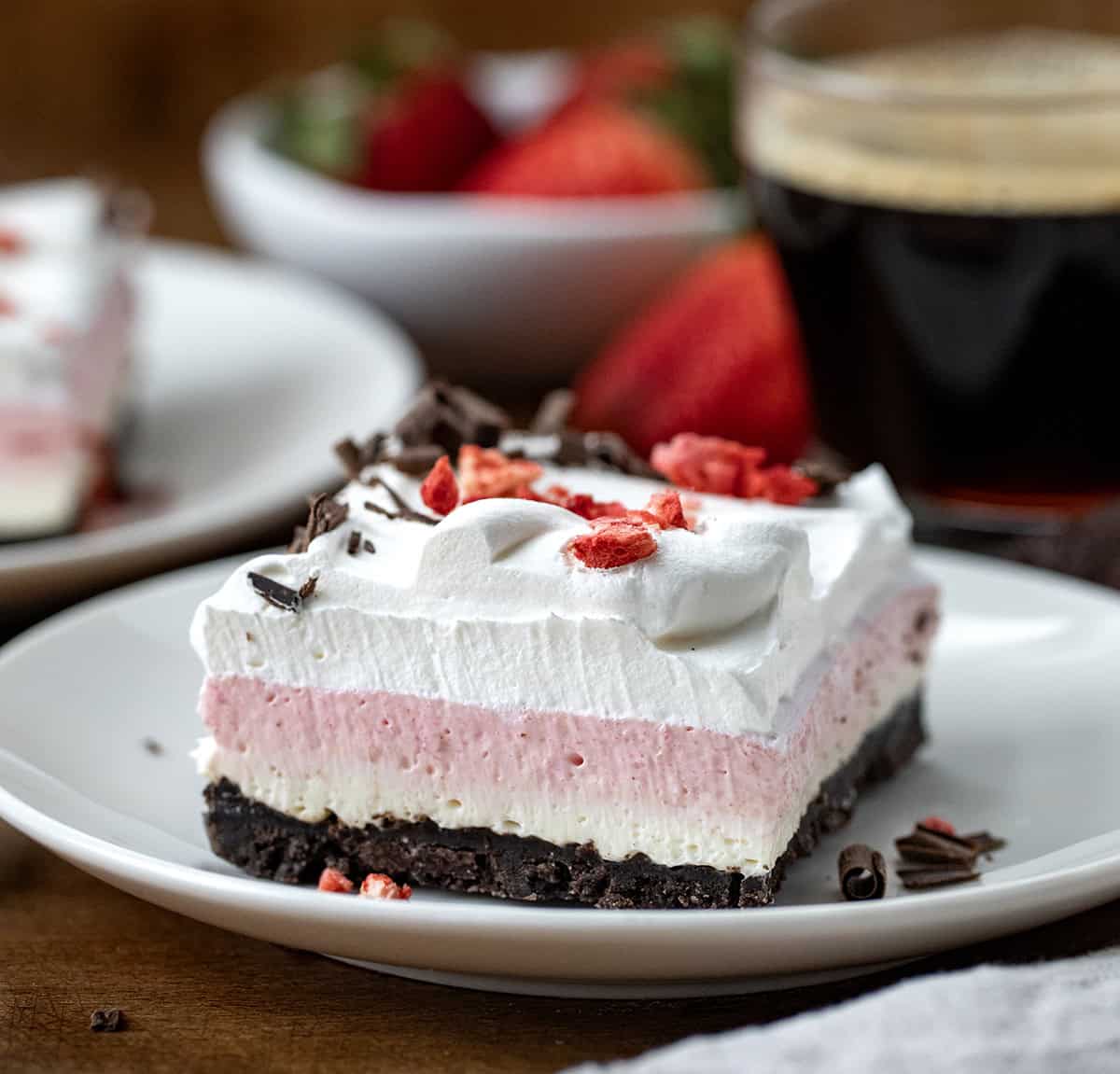 Triple layer Neapolitan Dessert on a white plate on a wooden table.