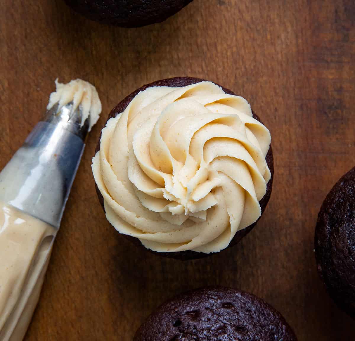 Looking down on a chocolate cupcake on a wooden table that is covered in piped Peanut Butter Frosting.