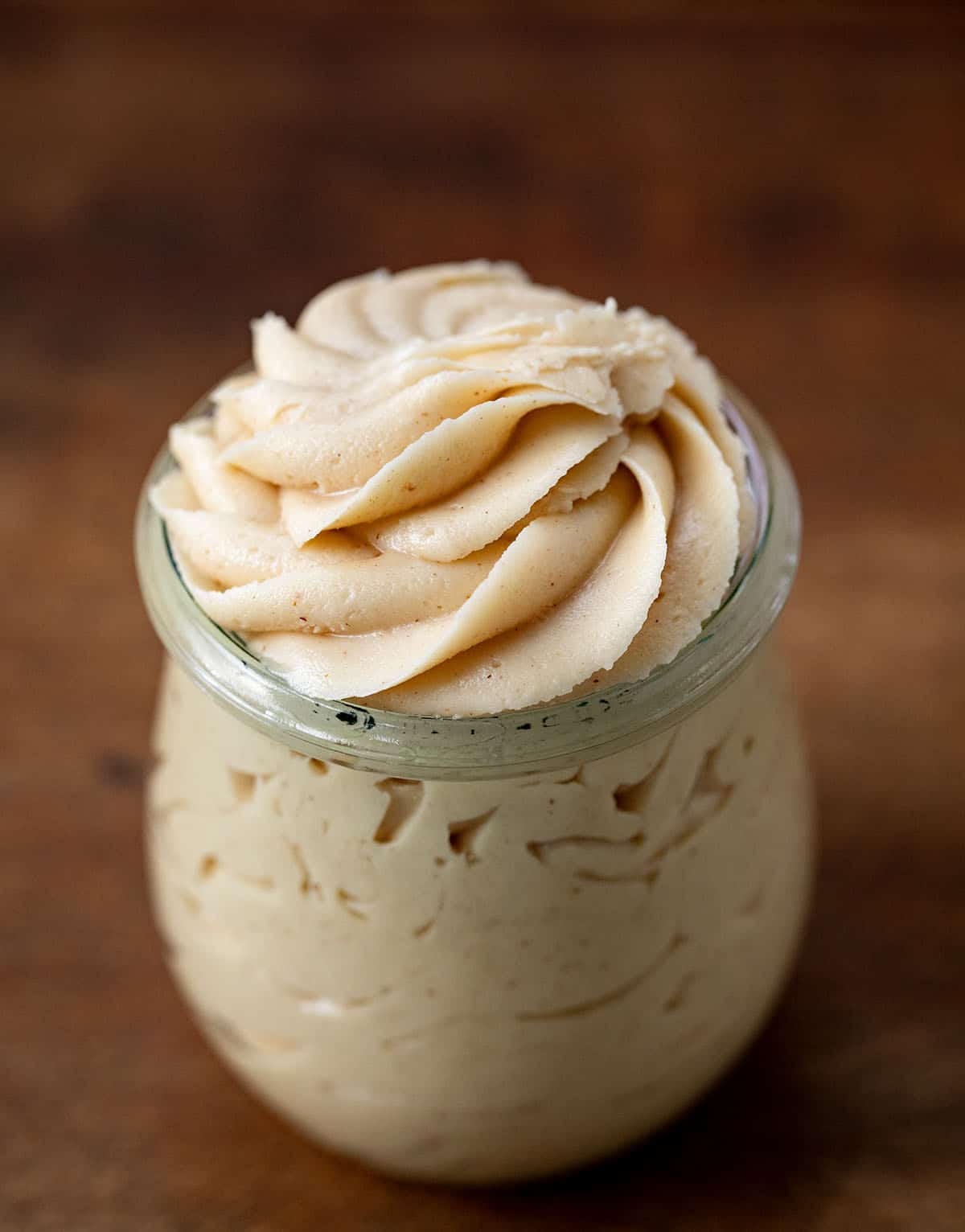 Jar of Peanut Butter Frosting on a wooden table. 