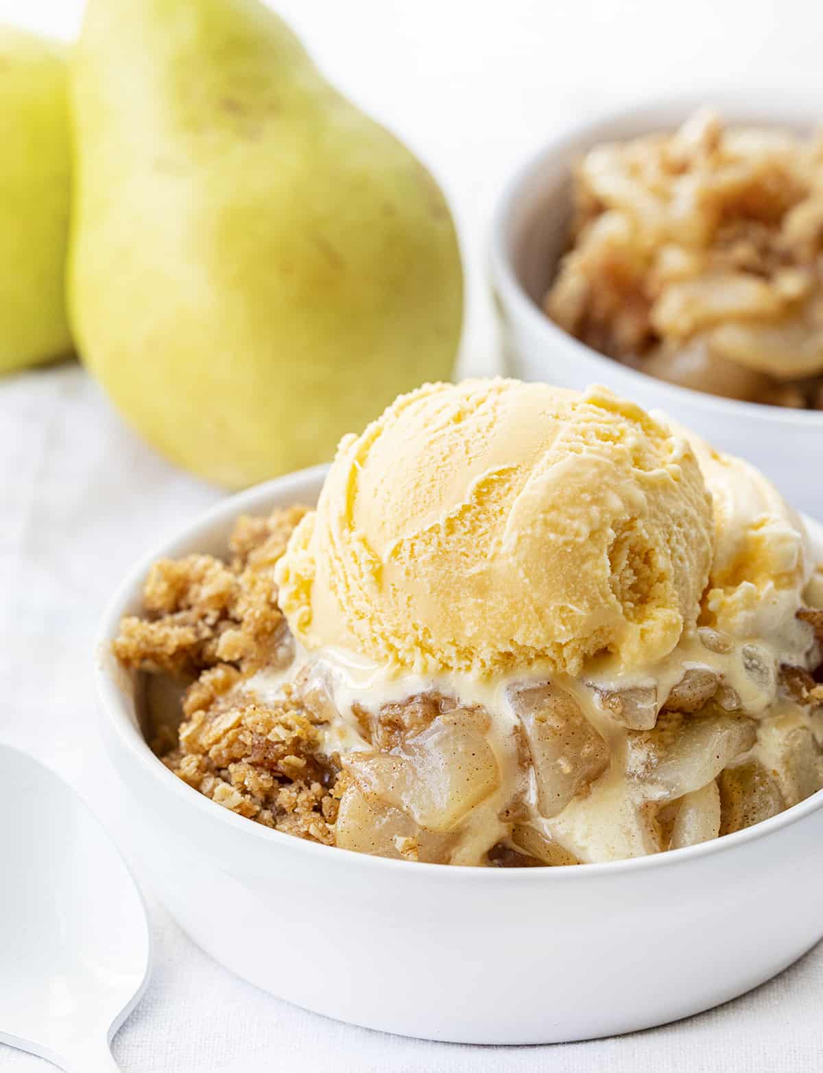 Bowl of Gingered Pear Crisp with Ice Cream and Pear in the Background. Dessert, Baking, Crisp, Best Crisp Recipes, Pear Crisp, Easy Pear Crisp, Holiday Desserts, Holiday Recipes, Old Fashioned Recipes, Historic Recipes, Grandma's Recipes, i am baker, iambaker