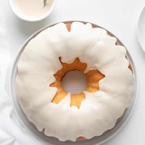 Whole Vanilla Bundt Cake on a White Cake Plate on a White Table from Overhead.