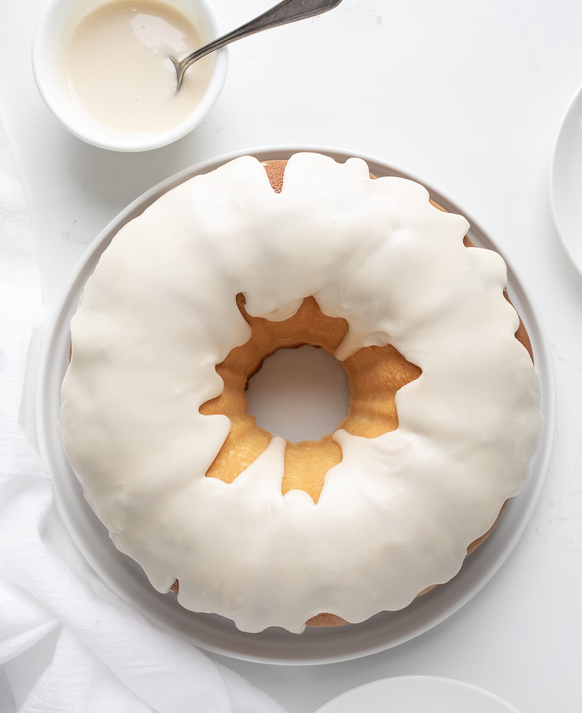 Whole Vanilla Bundt Cake on a White Cake Plate on a White Table from Overhead. 