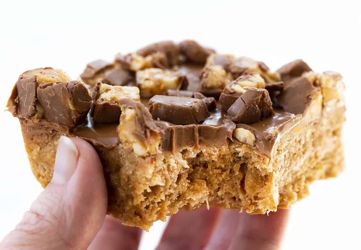 Snickers Special K Bar held by a hand and with a Bite taken out. Dessert, Scootchero Bars, SpecialK Bars, bars, bar recipes, scootch-er-oo bars, snicekrs bars, kid snacks, chocolate, peanut butter, butterscotch, recipes, i am baker, iambaker.