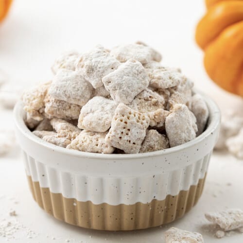 Bowl of Pumpkin Spice Puppy Chow (or Pumpkin Spice Muddy Buddies) with Mini Pumpkins in the Background.