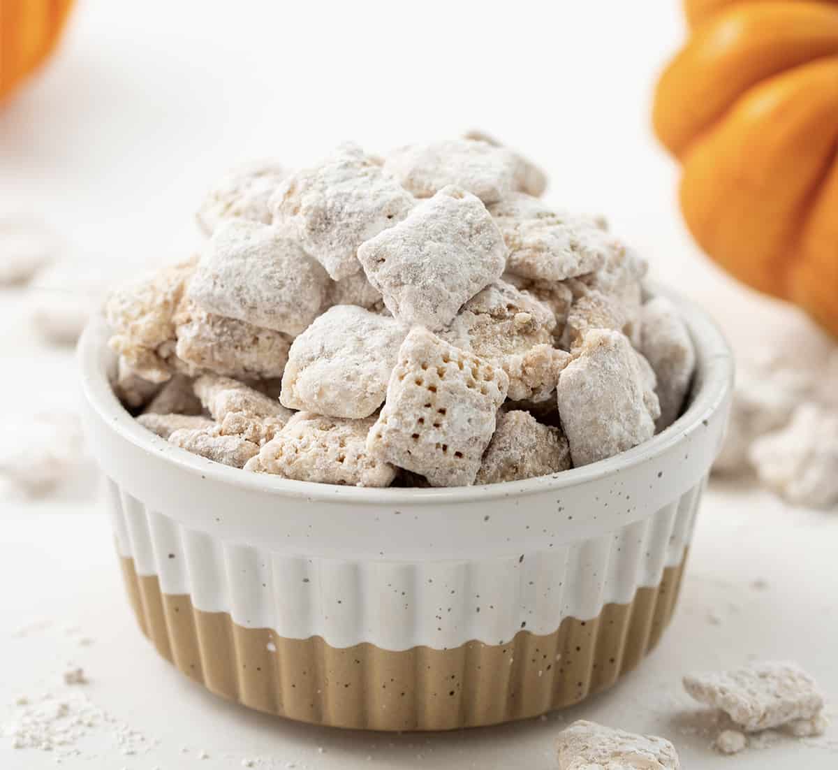 Bowl of Pumpkin Spice Puppy Chow (or Pumpkin Spice Muddy Buddies) with Mini Pumpkins in the Background.