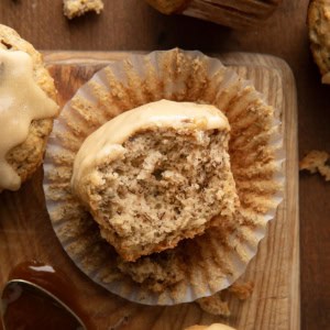 Halved Banana Muffin With Vanilla Caramel Glaze in its wrapper on a wooden table from overhead.