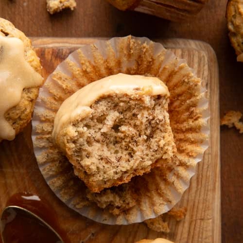 Halved Banana Muffin With Vanilla Caramel Glaze in its wrapper on a wooden table from overhead.