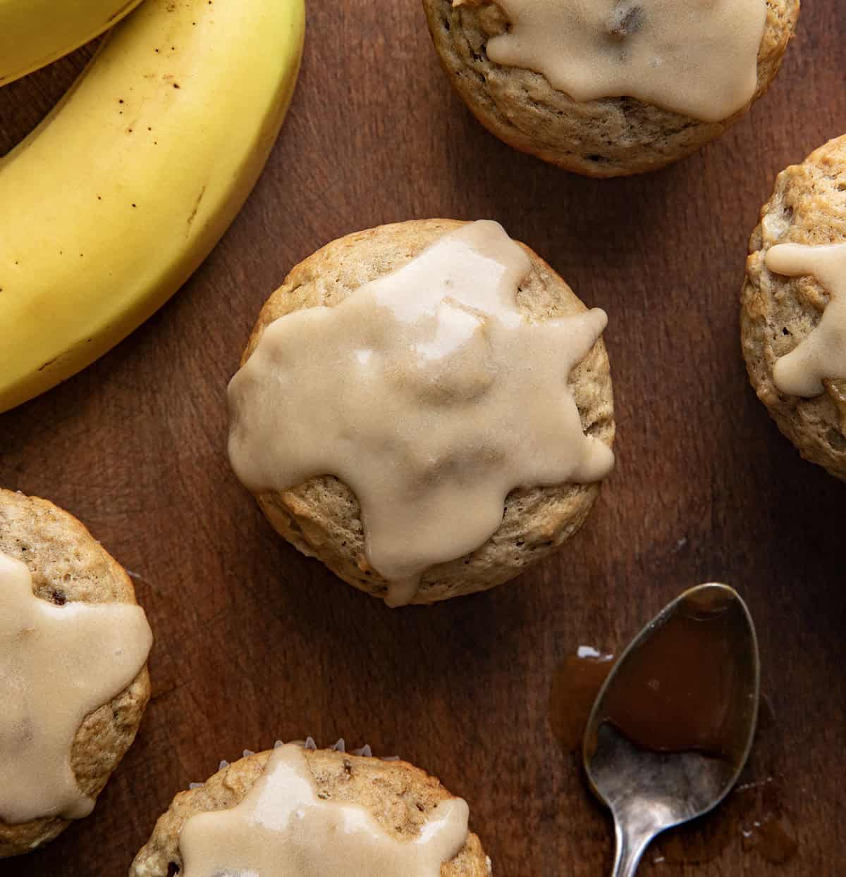 Banana Muffins With Vanilla Caramel Glaze on a wooden table from overhead with a banana and a spoon of caramel.