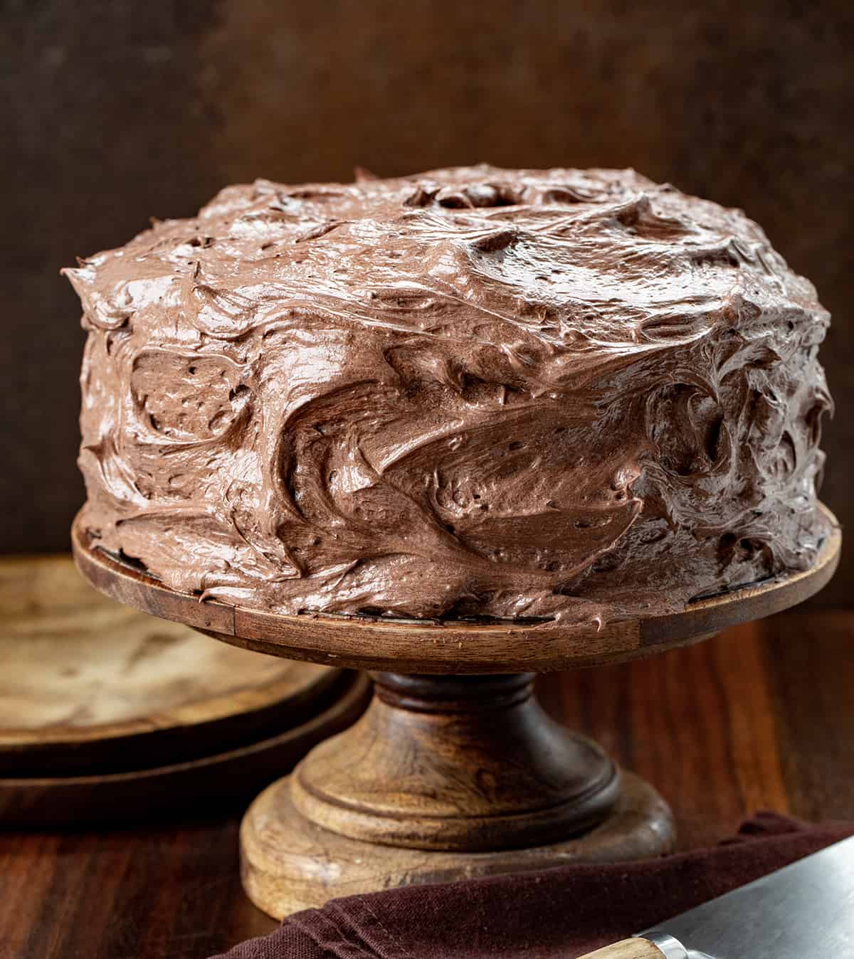Cake on a Wooden Cake stand Covered in Chocolate Ermine Frosting.
