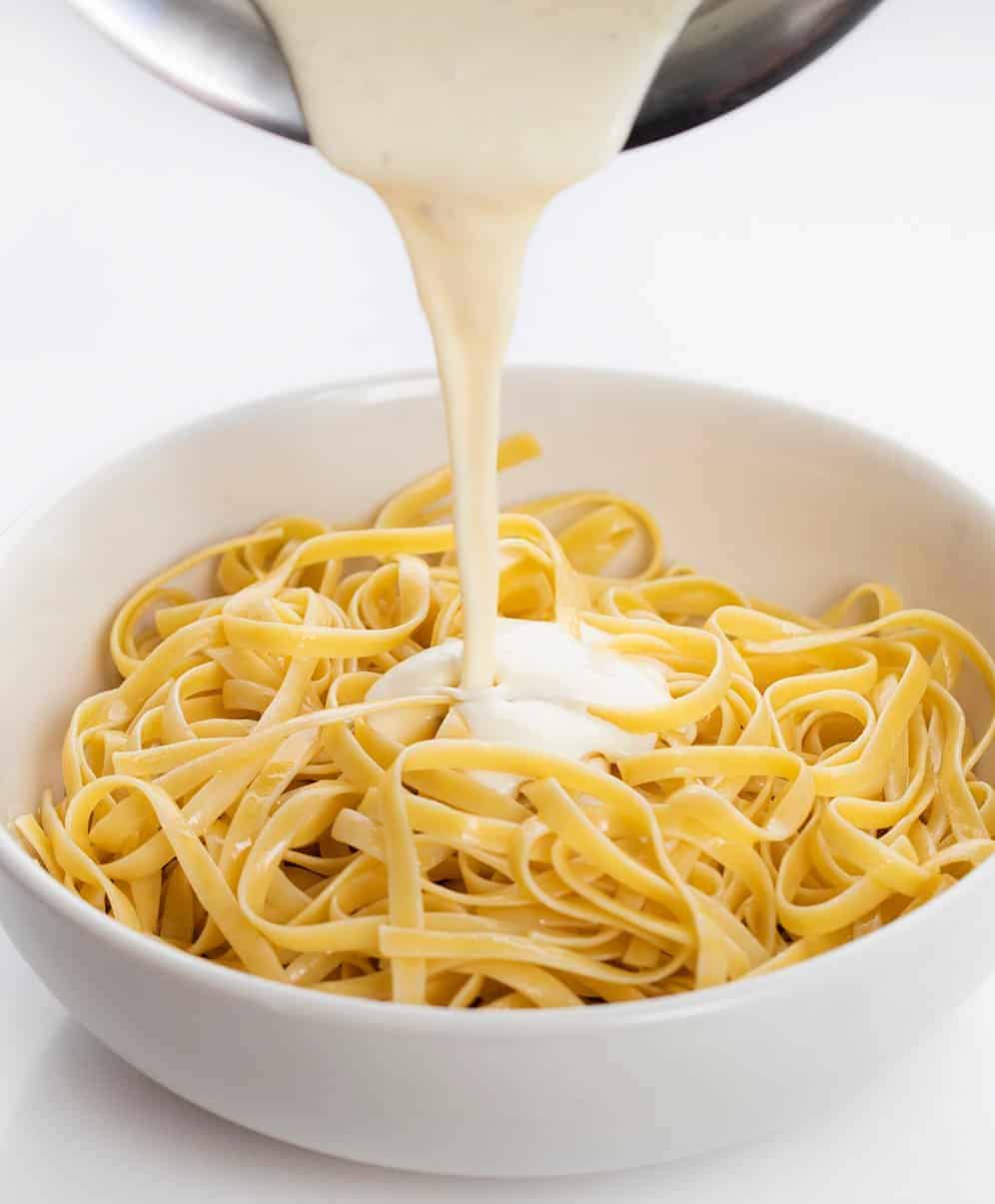 Pouring Alfredo over Fettuccini Noodles