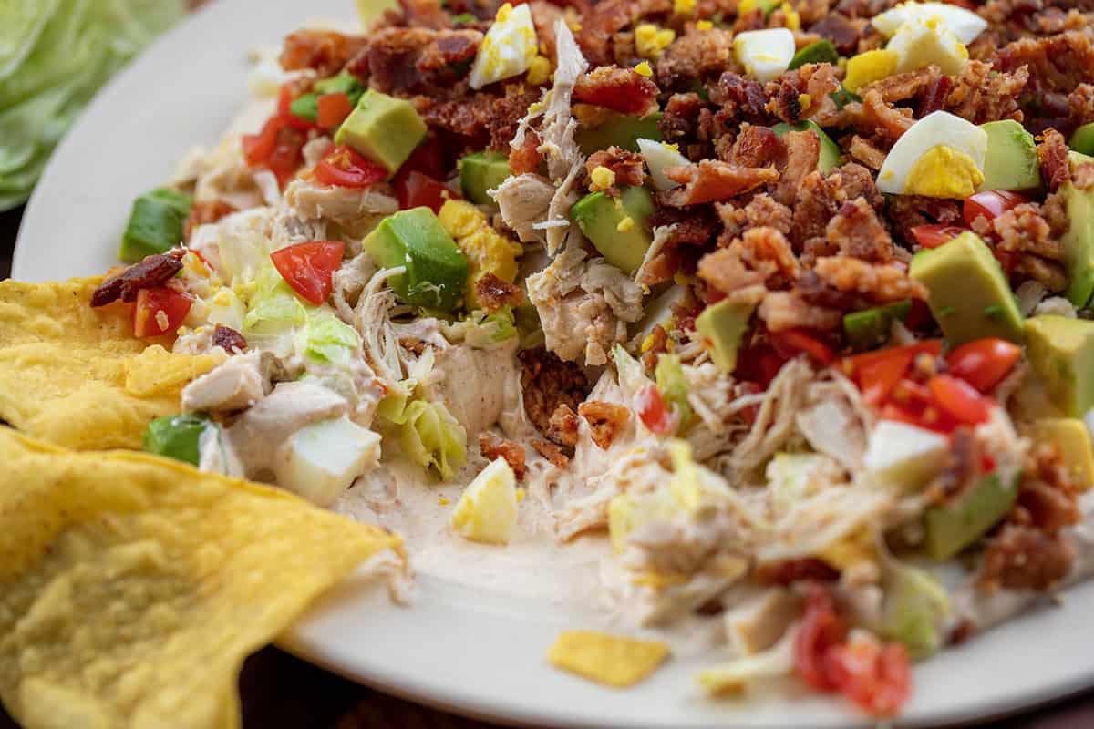 Close up of Southwest Cobb Salad Dip with a chip resting on the plate.