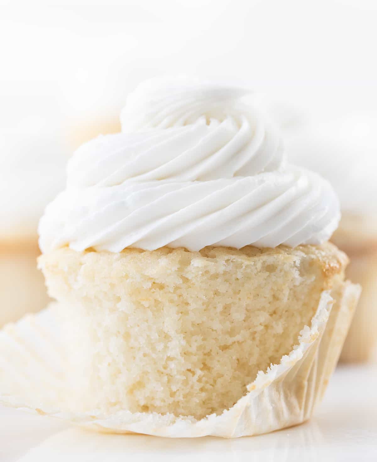 White Cupcake with Wrapper Removed Showing Texture of Cupcake and Covered in Vanilla Frosting.