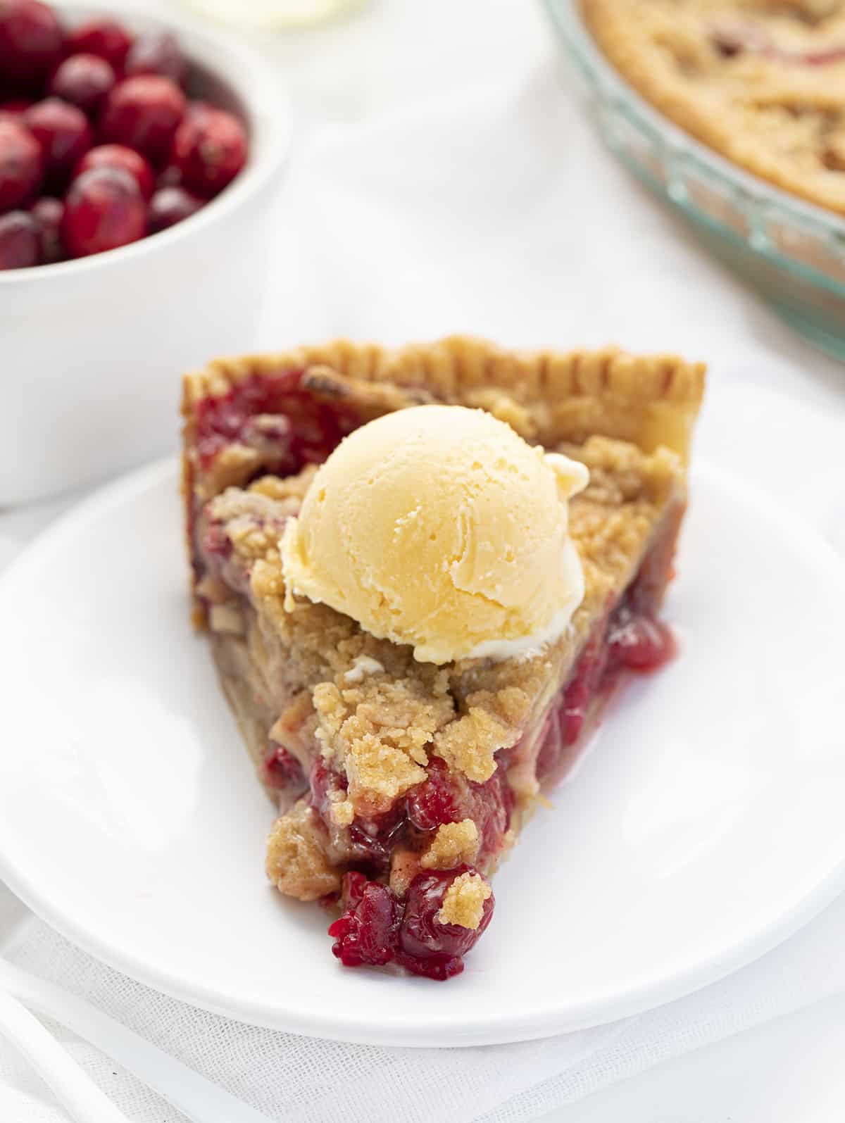 Slice of French Apple Cranberry Pie on a White PLate with Ice Cream and Cranberries in the Background. Dessert, Baking, Pies, French Pies, Cranberry Pie, Apple Pie, Crumble for Pie, Homemade Pie, Holiday Pie, Christmas Pie, Thanksgiving Pie, Thanksgiving Dessert, Christmas Dessert, i am baker, iambaker