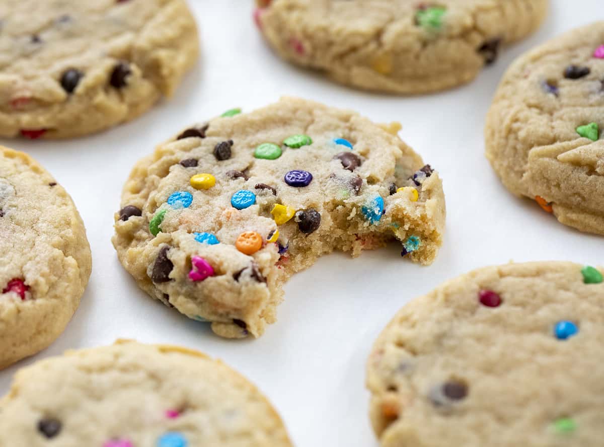 Rainbow Chip Cookies on White Counter with a Cookie that Has a Bite Taken Out of It. Baking, Cookies, Cookie Recipes, Dessert, Rainbow Chip, Rainbow Cookies, Rainbow Chip Chocolate Chip Cookies, Soft Cookies, Chewy Cookies, Cookie Dough, i am baker, iambaker