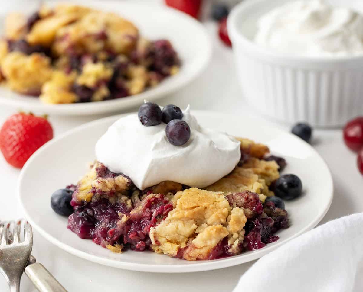 Fruit cobbler on a white plate with whipped cream and blueberries.
