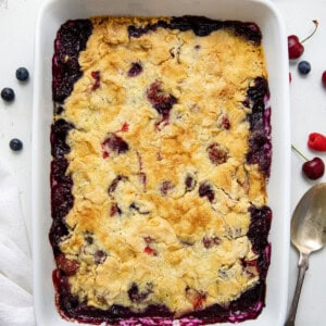 Pan of fruit cobbler on a white table with cherries and raspberries and blueberry from overhead.