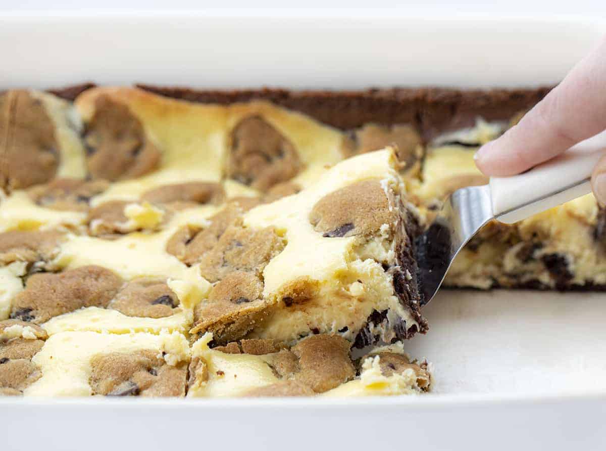 Hand holding a Spatula picking up a Chocolate Chip Cookie Cheesecake Brownies from the pan