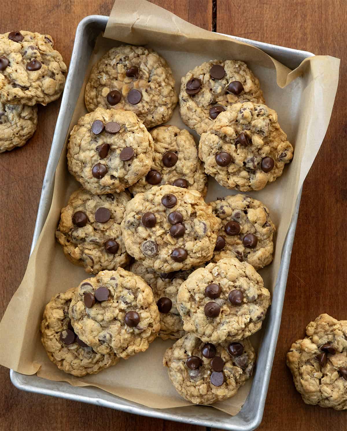 Oatmeal Chocolate Chip Cookies in a pan with tan parchment paper on a wooden table.