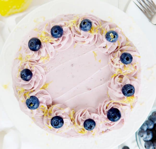 Overhead view of a lemon cake covered in blueberry buttercream, blueberries, and lemon zest.