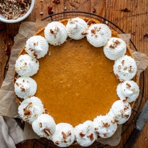 Whole Pumpkin Cheesecake on a Wooden Table with Nuts and Silverware Around from Overhead.