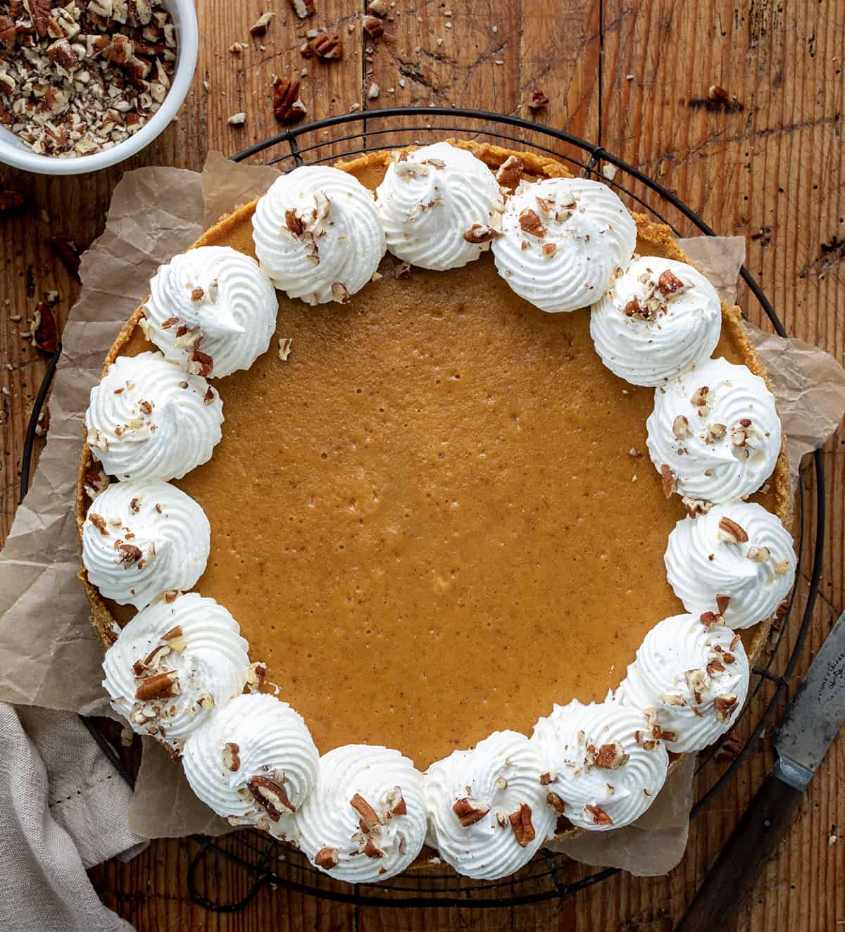 Whole Pumpkin Cheesecake on a Wooden Table with Nuts and Silverware Around from Overhead.