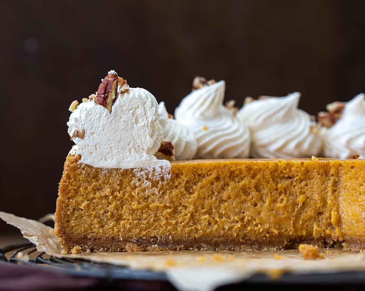 A Whole Pumpkin Cheesecake on a Rack with Pieces Removed Showing the Inside Texture.