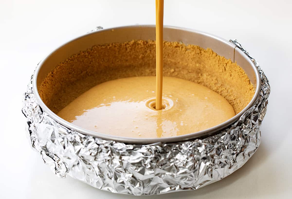 Pouring Pumpkin Cheesecake Filling into Springform Pan That is Wrapped in Foil.