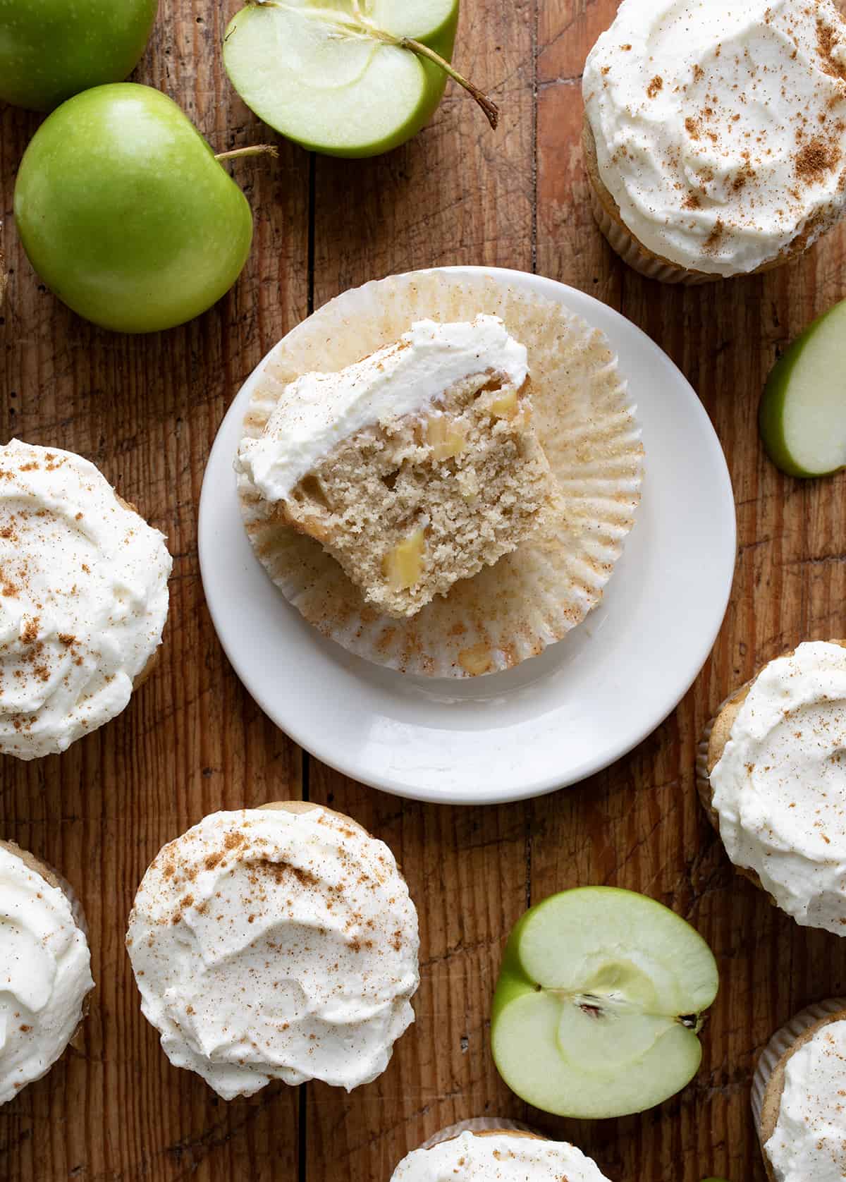 Apple Pie Cupcake Cut in Half on a Plate Surrounded by More Apple Pie Cupcakes and apples from Overhead.