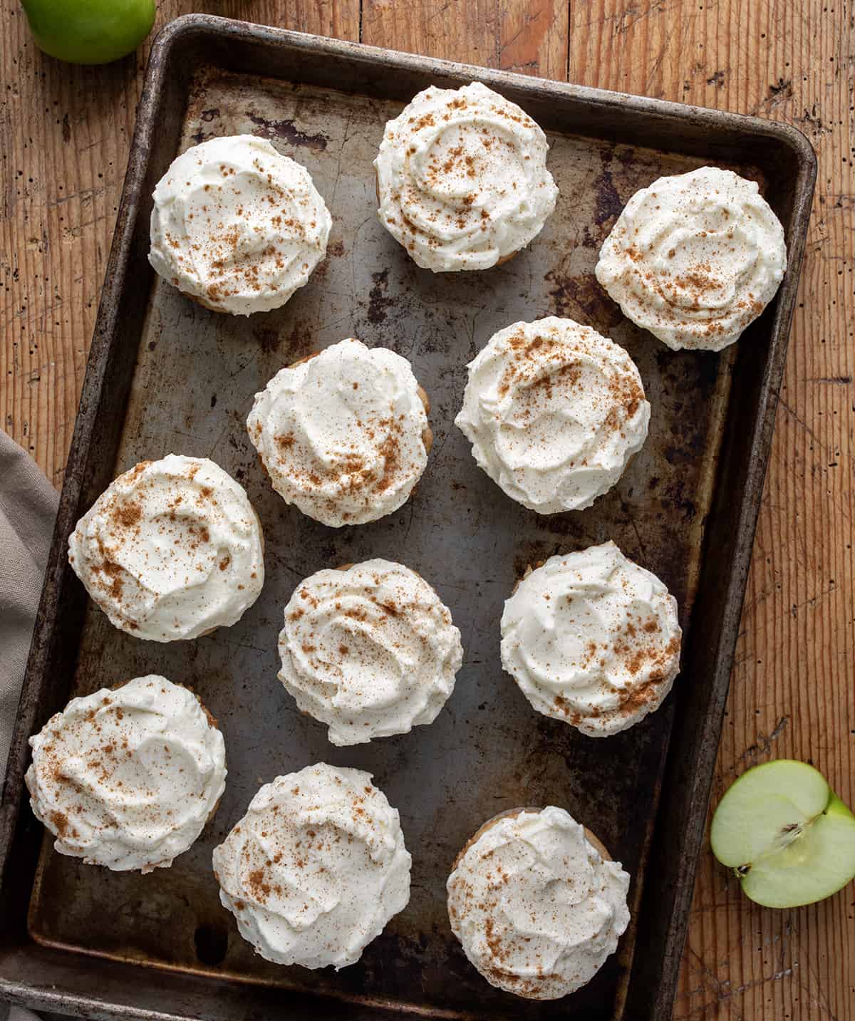Apple Pie Cupcakes are perfectly spiced, tender cupcakes baked with apple pie filling and topped with stabilized whipped cream. So tender and delicious! They are reminiscent of a slice of apple pie but in convenient cupcake form! Tray of Apple Pie Cupcakes on a Table with Apples.