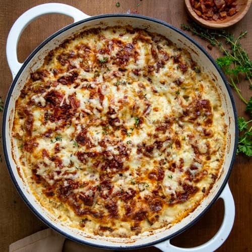 White Skillet of Gruyere Scalloped Potatoes on a wooden table from overhead.