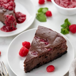 Slices of Chocolate Raspberry Cheesecake on white plates on a white counter.