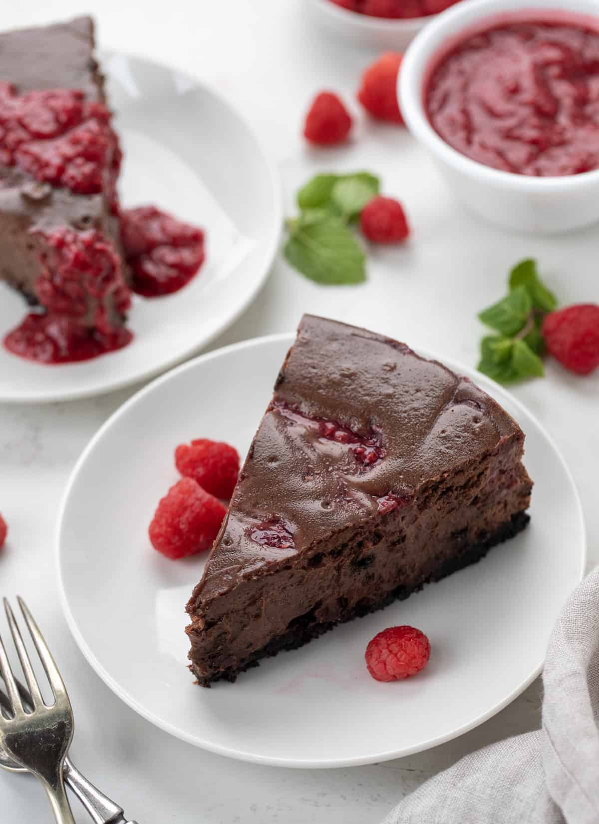 Slices of Chocolate Raspberry Cheesecake on white plates on a white counter.