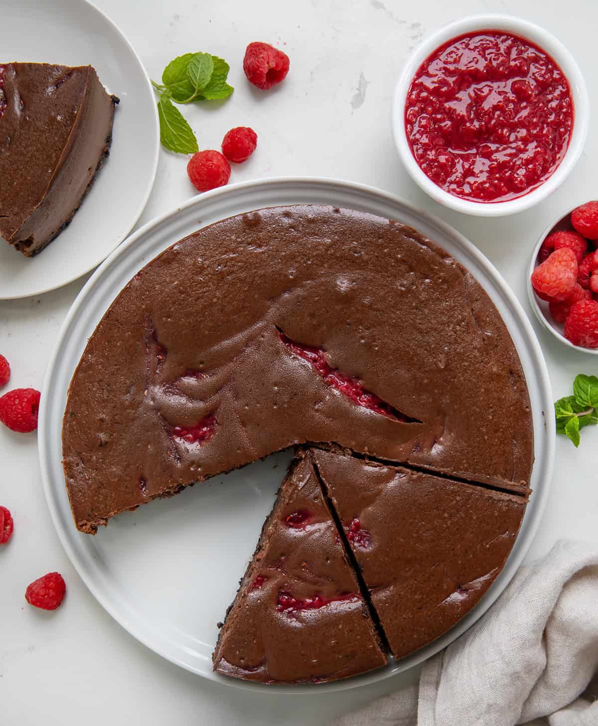 Chocolate Raspberry Cheesecake on a white serving platter with some slices cut on white plates from overhead.