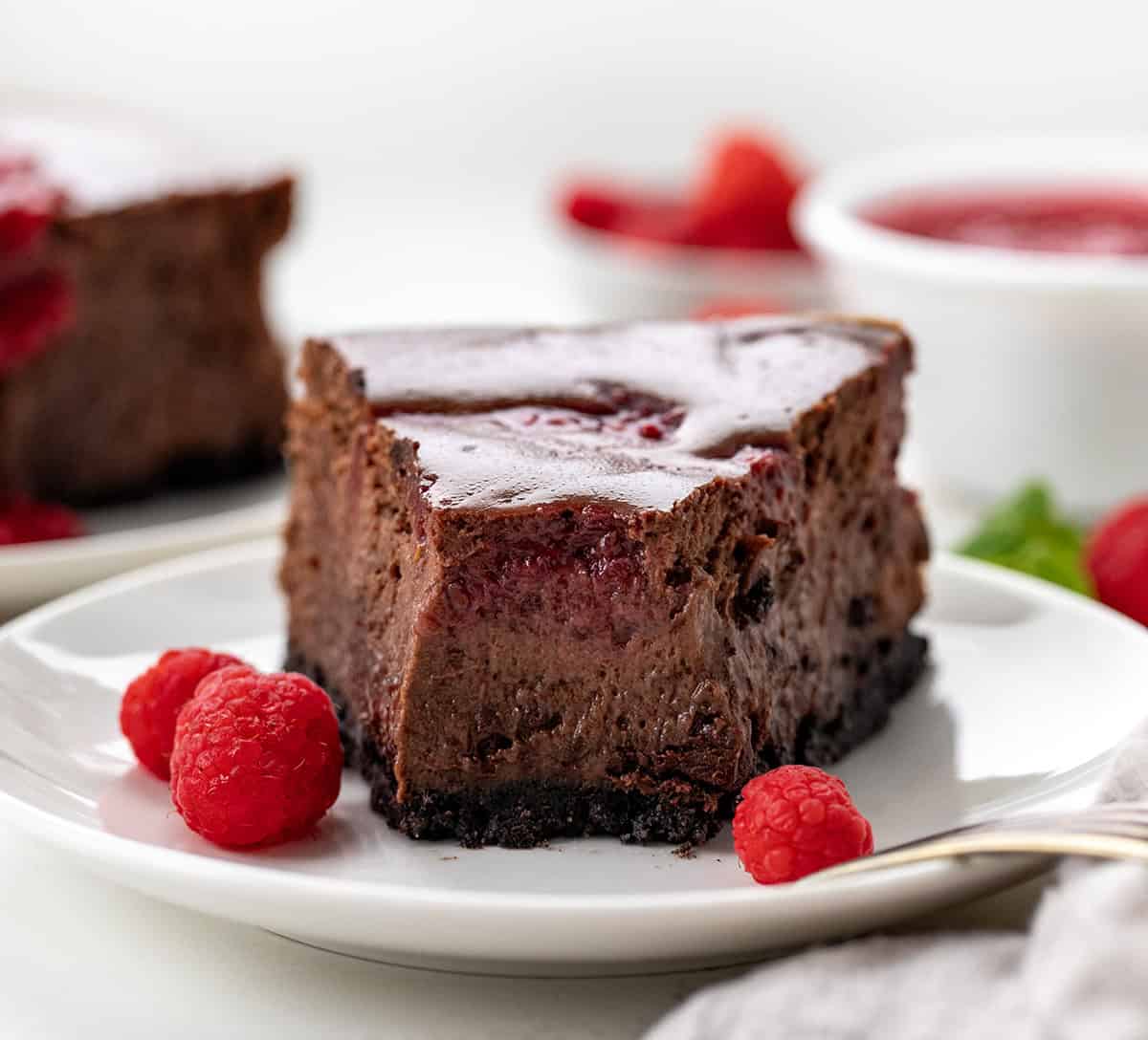 One piece of Cheesecake on a white plate with a bite taken out showing tender creamy chocolate raspberry cheesecake.