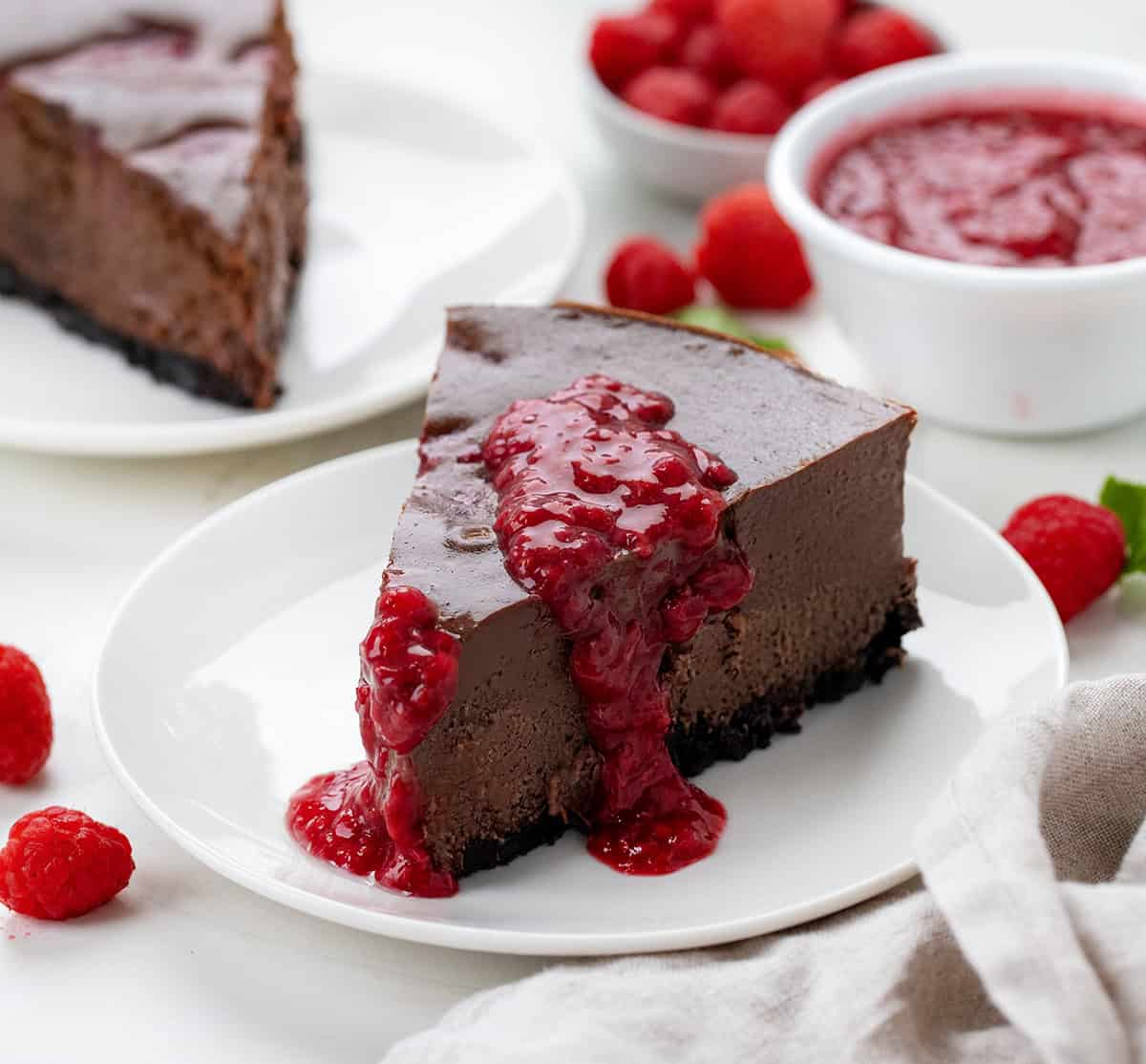 Pieces of Chocolate Raspberry Cheesecake on white plates on a white table.