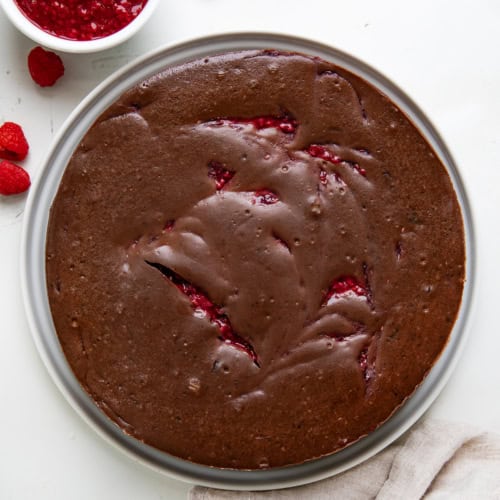 Whole Chocolate Raspberry Cheesecake on a white platter on a white table from overhead.